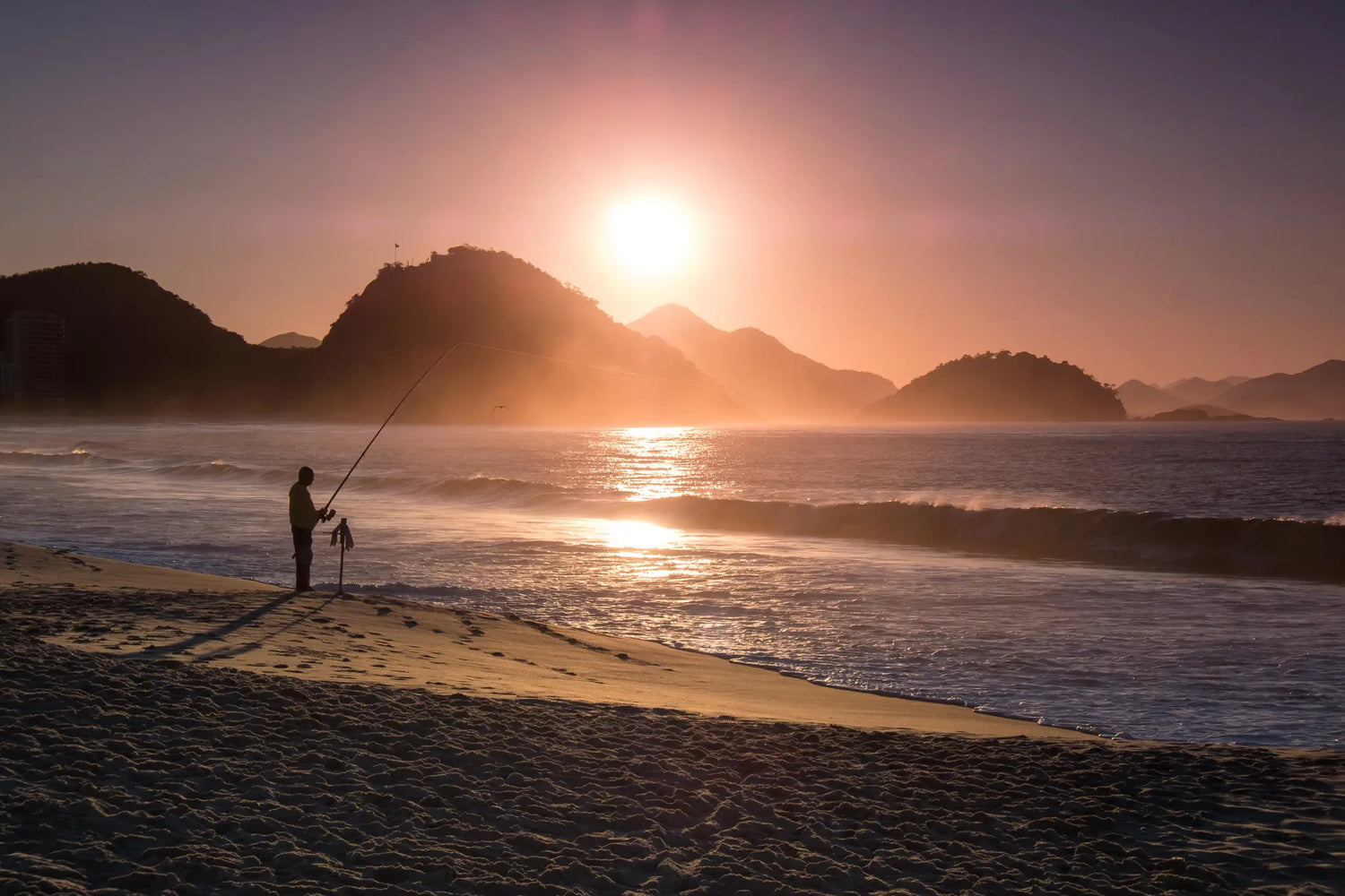 Man fishing on a beach at sunset